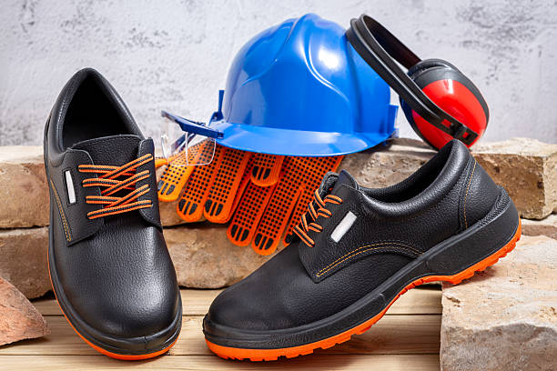Construction safety equipment. Work shoes, protective gloves, safety helmet, ear protection and goggles leaning against old bricks lined up on a wooden table.